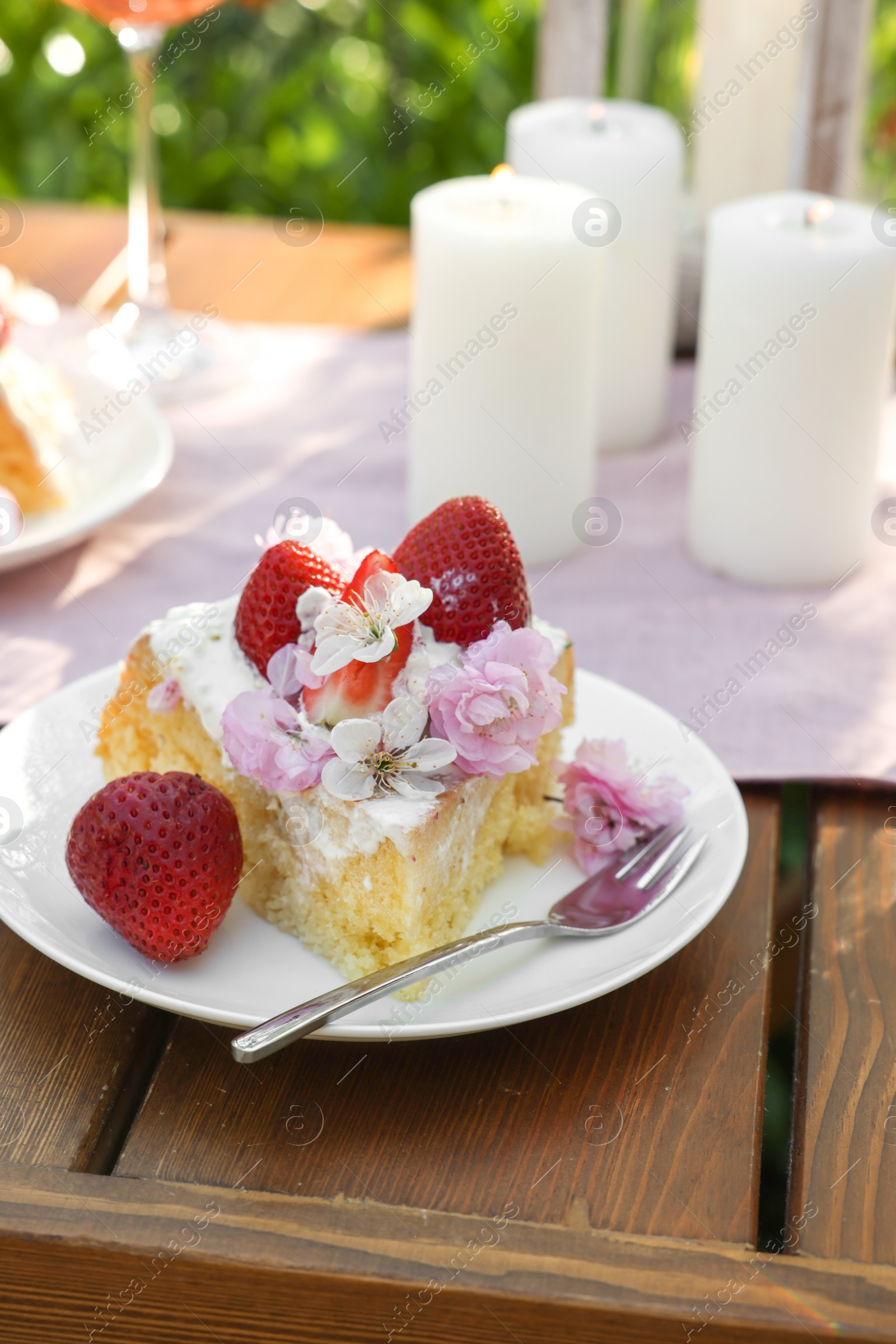 Photo of Piece of delicious homemade cake decorated with fresh strawberries and candles on table outdoors, closeup