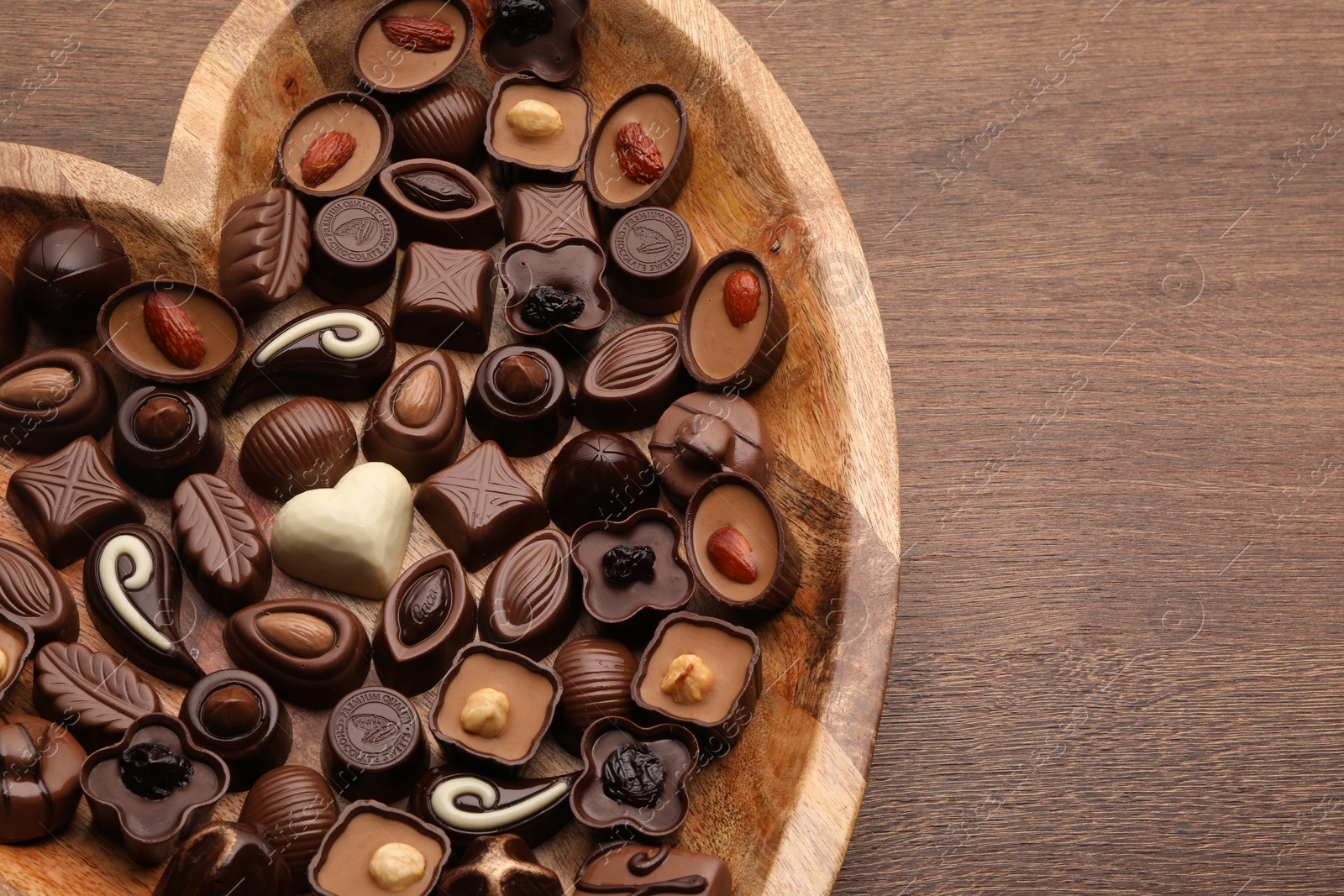 Photo of Heart shaped plate with delicious chocolate candies on wooden table, top view