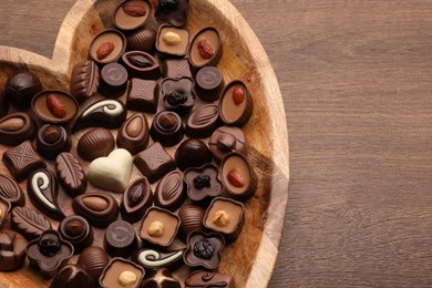 Heart shaped plate with delicious chocolate candies on wooden table, top view