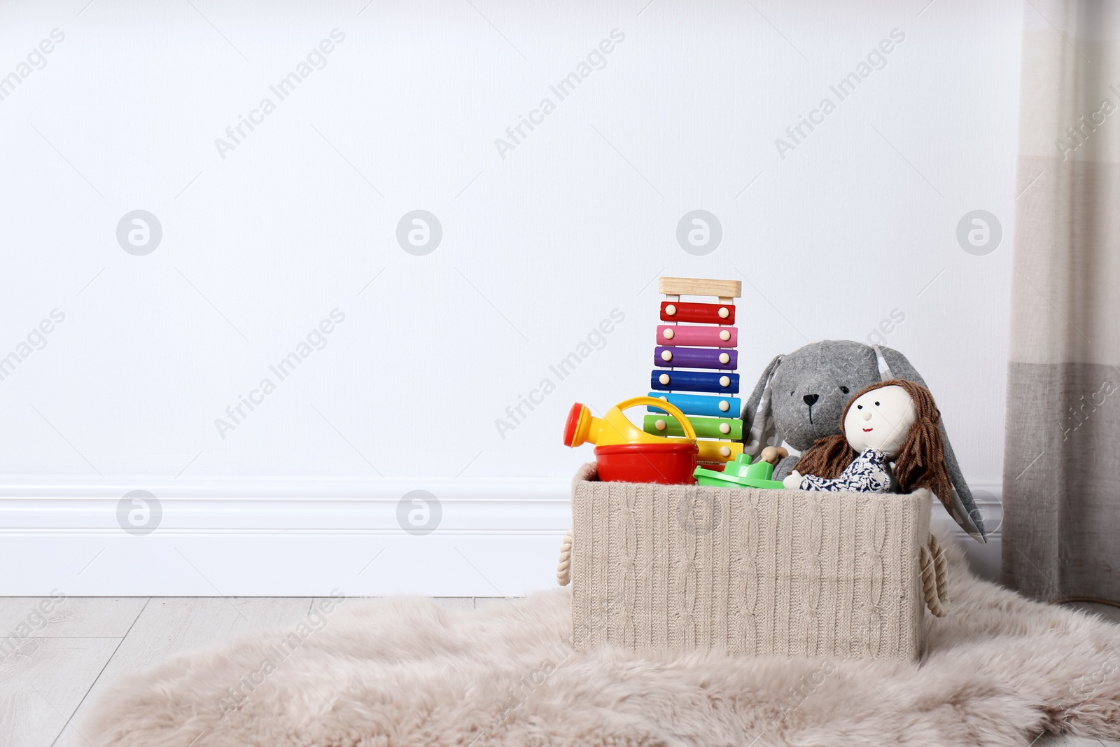 Photo of Box with different child toys on floor against white wall. Space for text