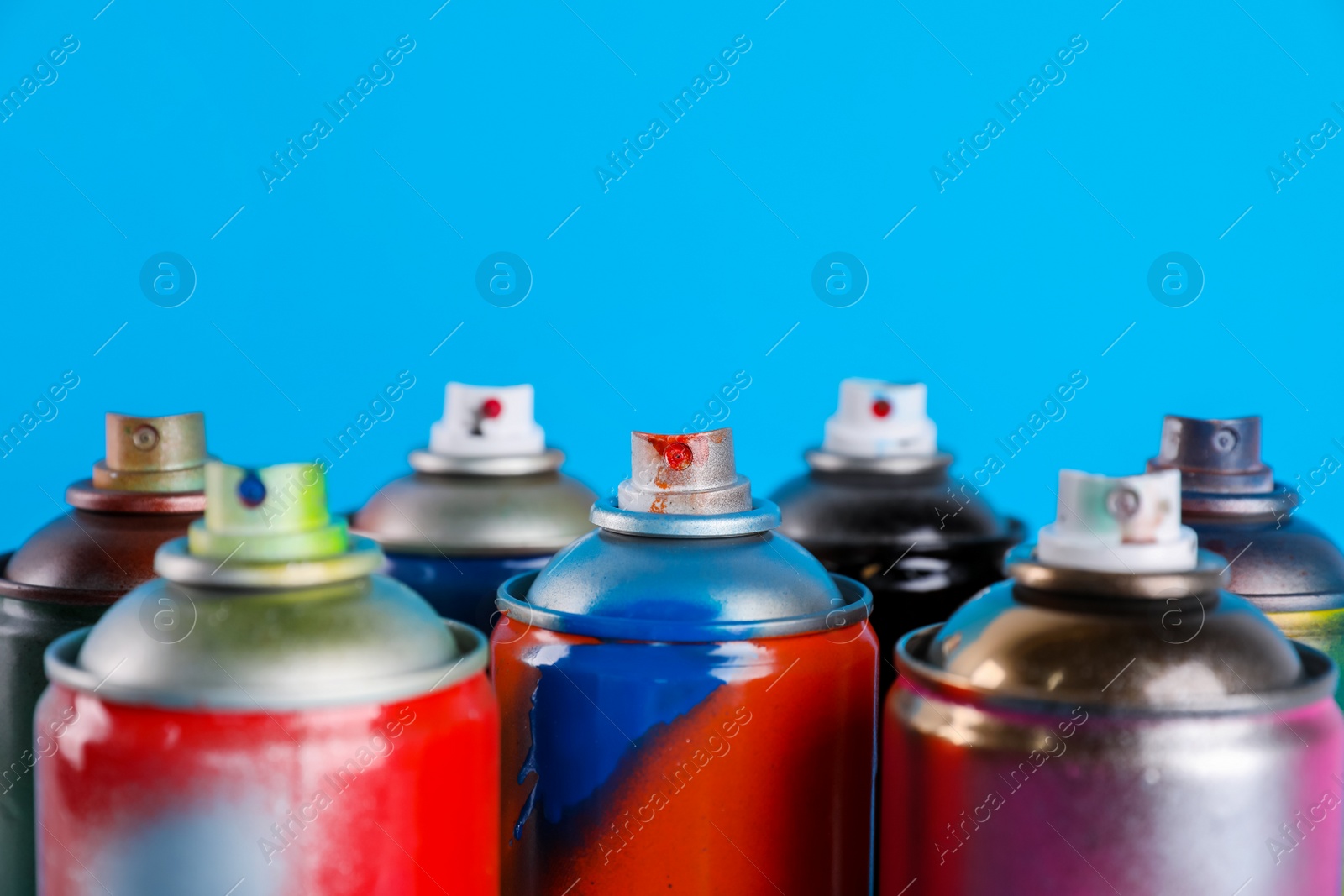 Photo of Used cans of spray paints on light blue background, closeup