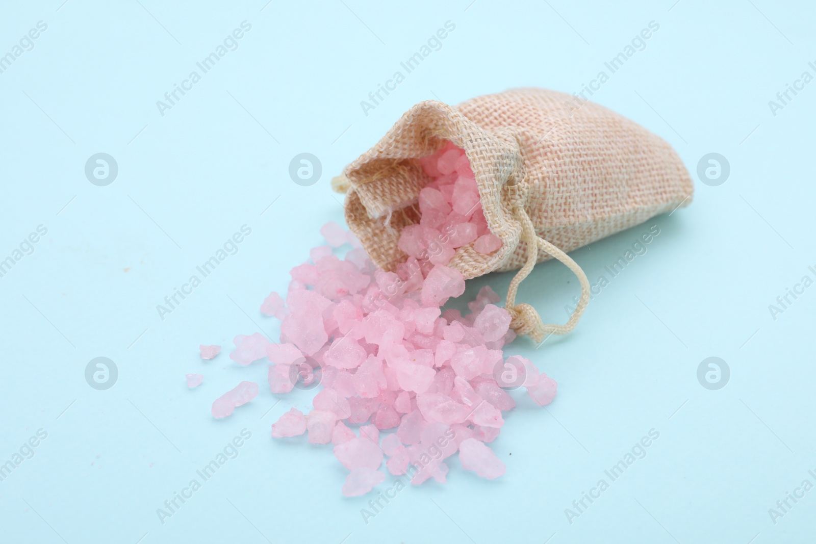 Photo of Bag with pink sea salt on light blue background