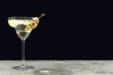 Martini cocktail with ice and olives on grey table against dark background. Space for text