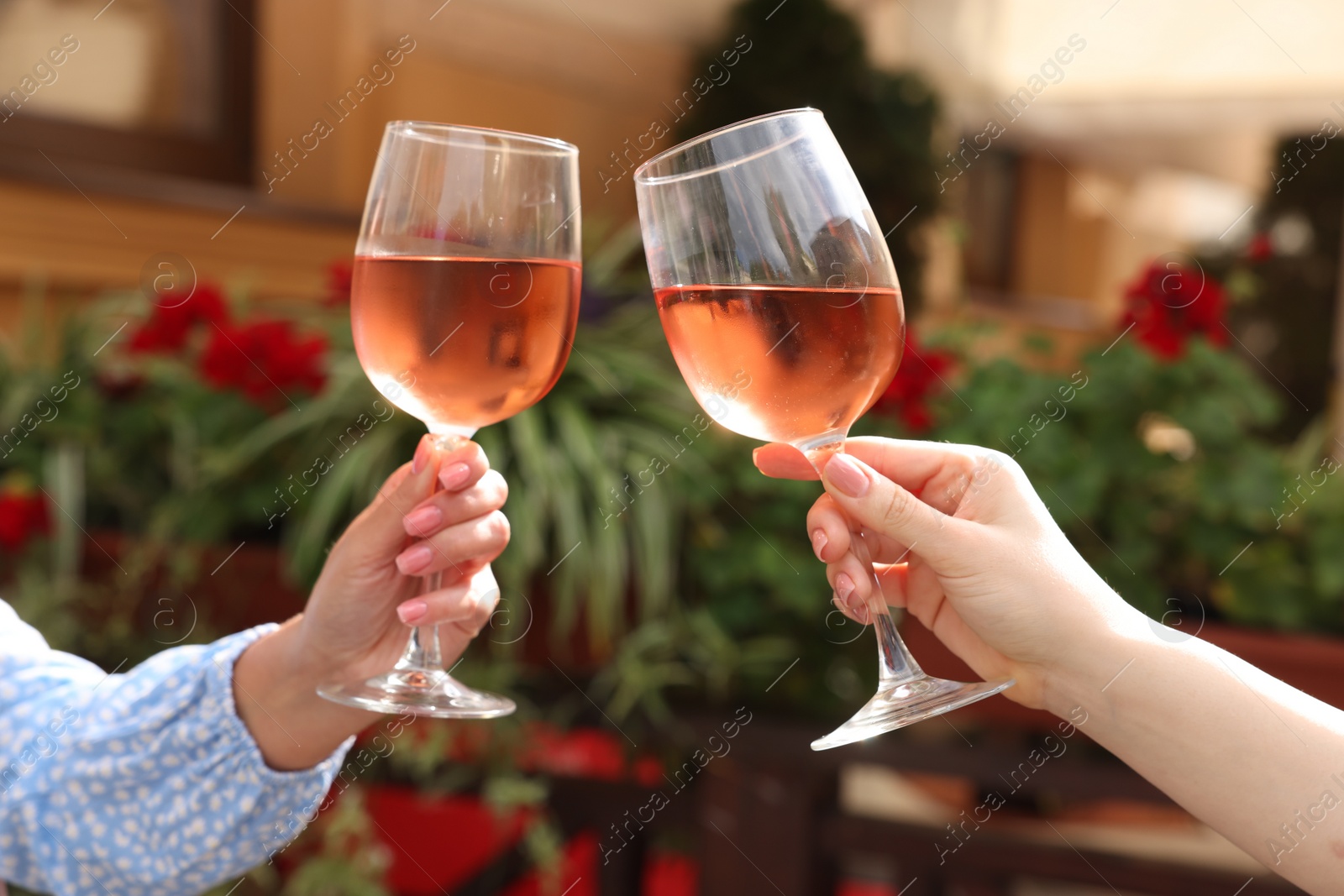 Photo of Women clinking glasses with rose wine in outdoor cafe, closeup