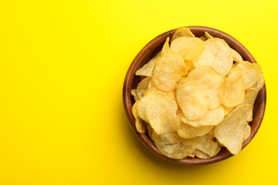 Delicious crispy potato chips in bowl on color background, top view with space for text