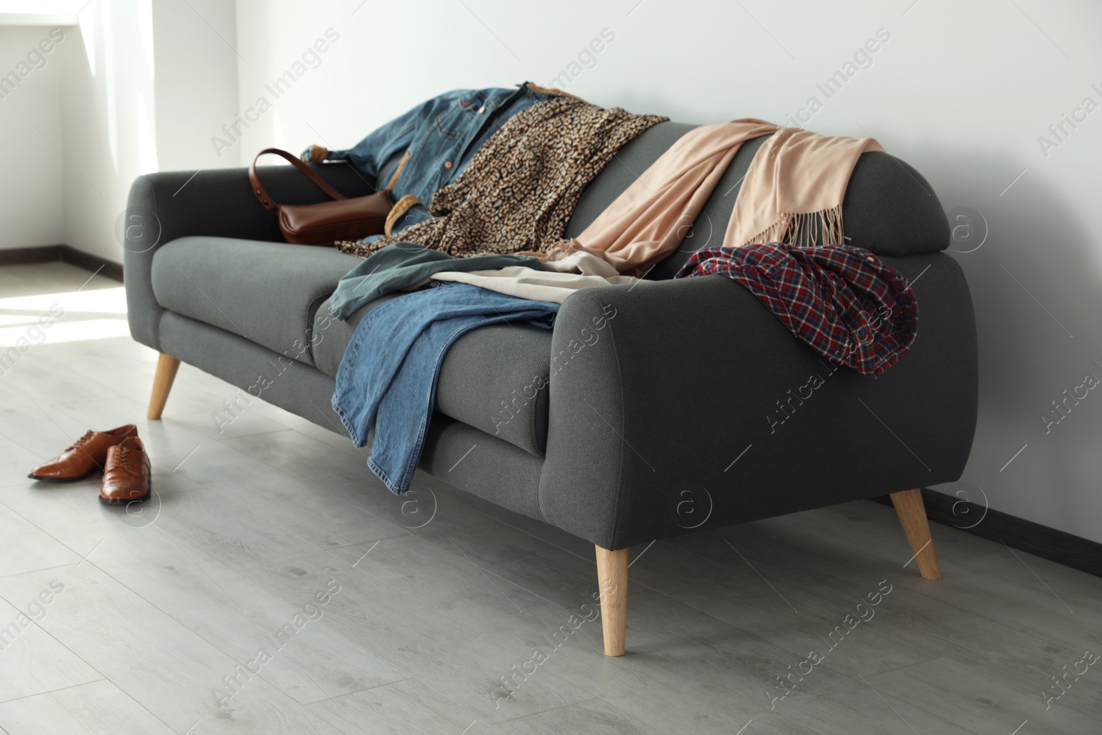 Photo of Messy pile of clothes on sofa and shoes in living room