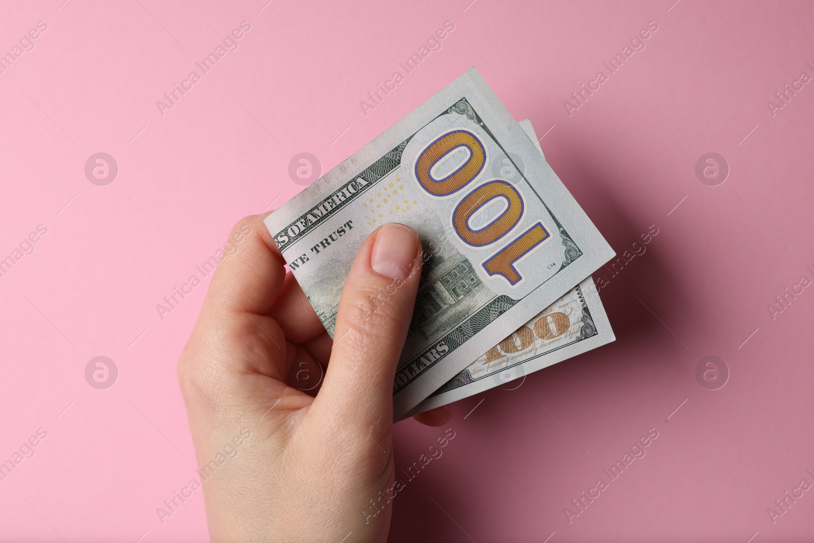 Photo of Money exchange. Woman holding dollar banknotes on pink background, top view