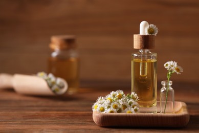 Photo of Chamomile essential oil and flowers on wooden table, space for text