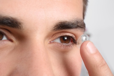 Photo of Young man putting contact lens into his eye, closeup