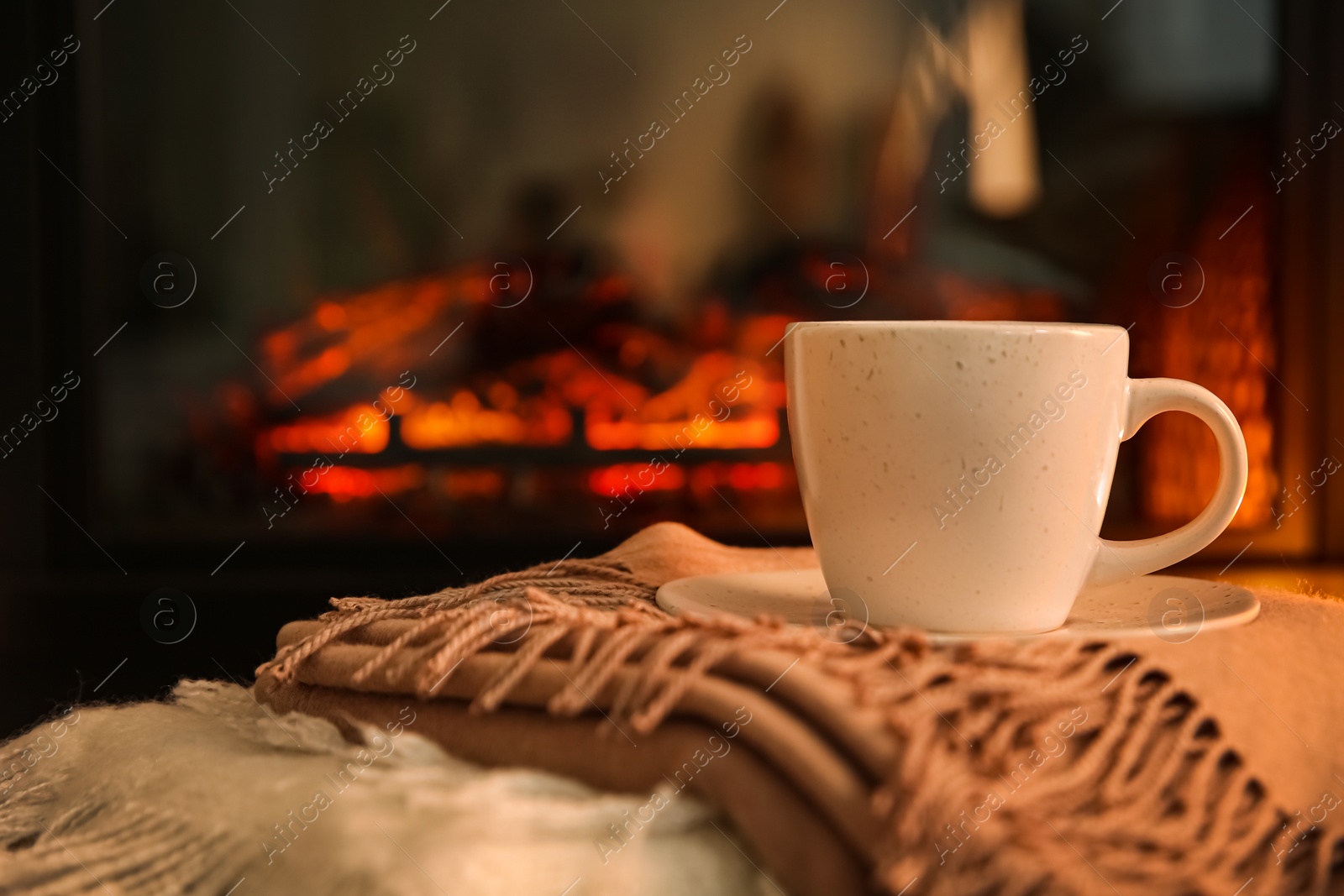Photo of Cup with hot drink on plaids against fireplace, space for text
