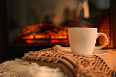 Photo of Cup with hot drink on plaids against fireplace, space for text