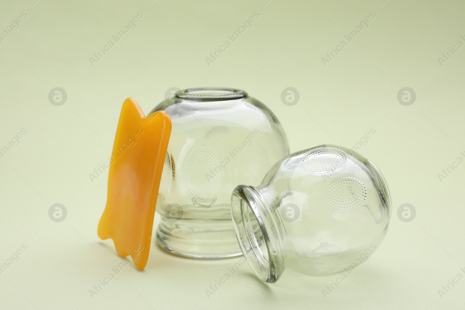 Photo of Glass cups and gua sha on light olive background, closeup. Cupping therapy