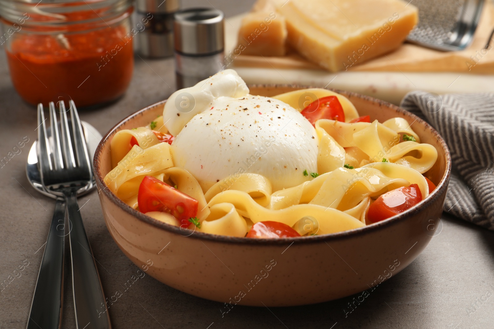 Photo of Bowl of delicious pasta with burrata and tomatoes on grey table