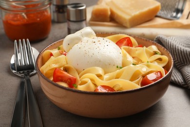 Photo of Bowl of delicious pasta with burrata and tomatoes on grey table