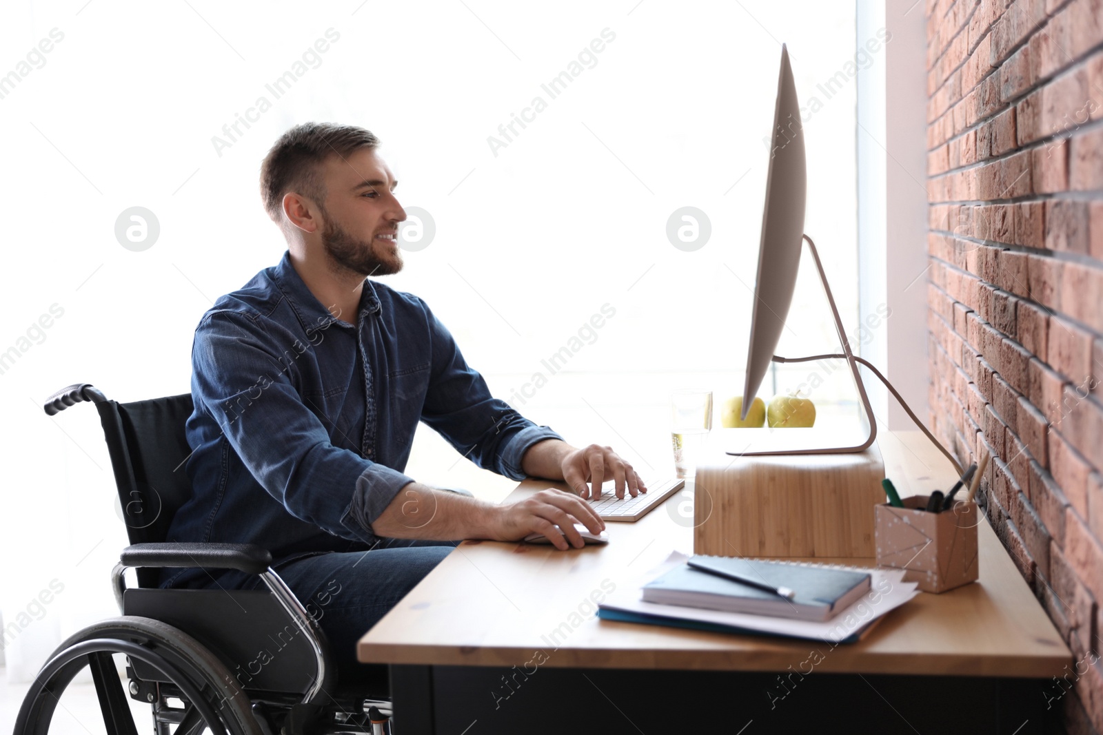 Photo of Man in wheelchair working with computer at table indoors