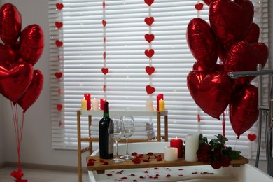 Wooden tray with wine, burning candles and rose petals on tub in bathroom. Valentine's day celebration