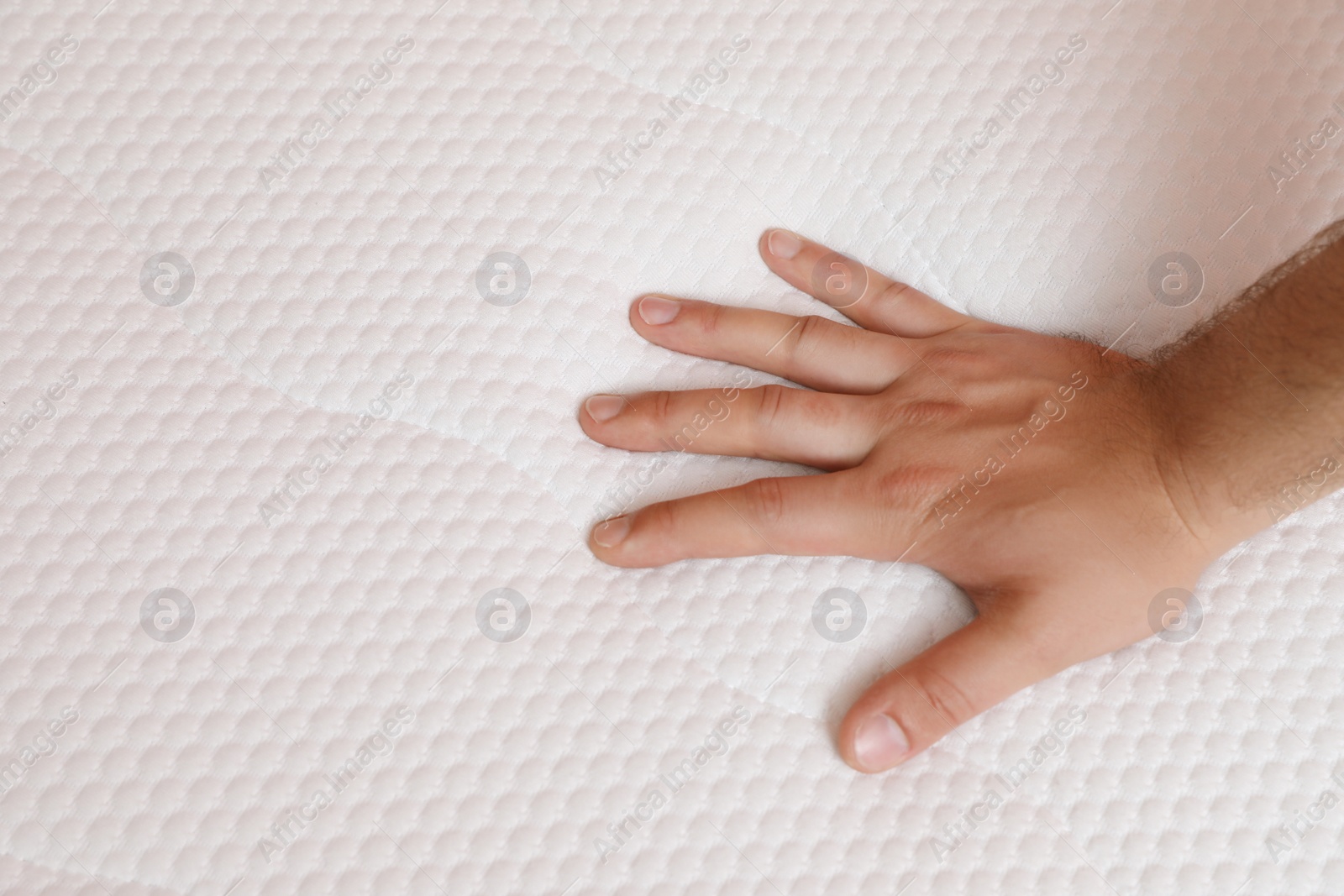 Image of Man checking firmness of mattress, closeup view