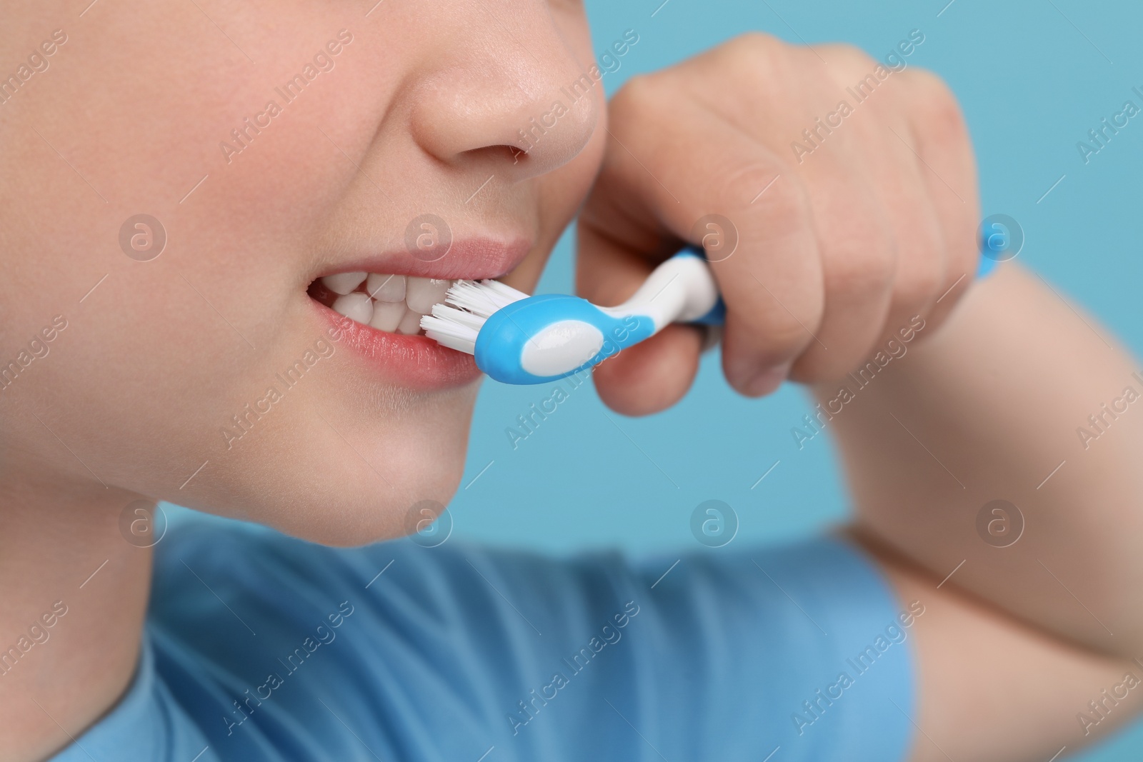 Photo of Girl brushing her teeth with toothbrush on light blue background, closeup