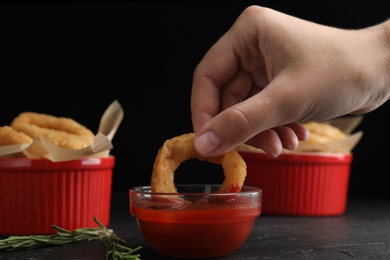 Photo of Woman dipping crunchy fried onion ring in tomato sauce on black background, closeup
