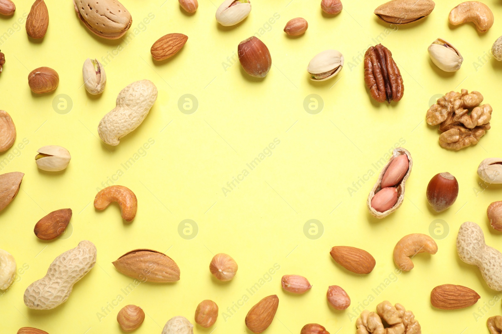 Photo of Different delicious nuts on yellow background, flat lay. Space for text