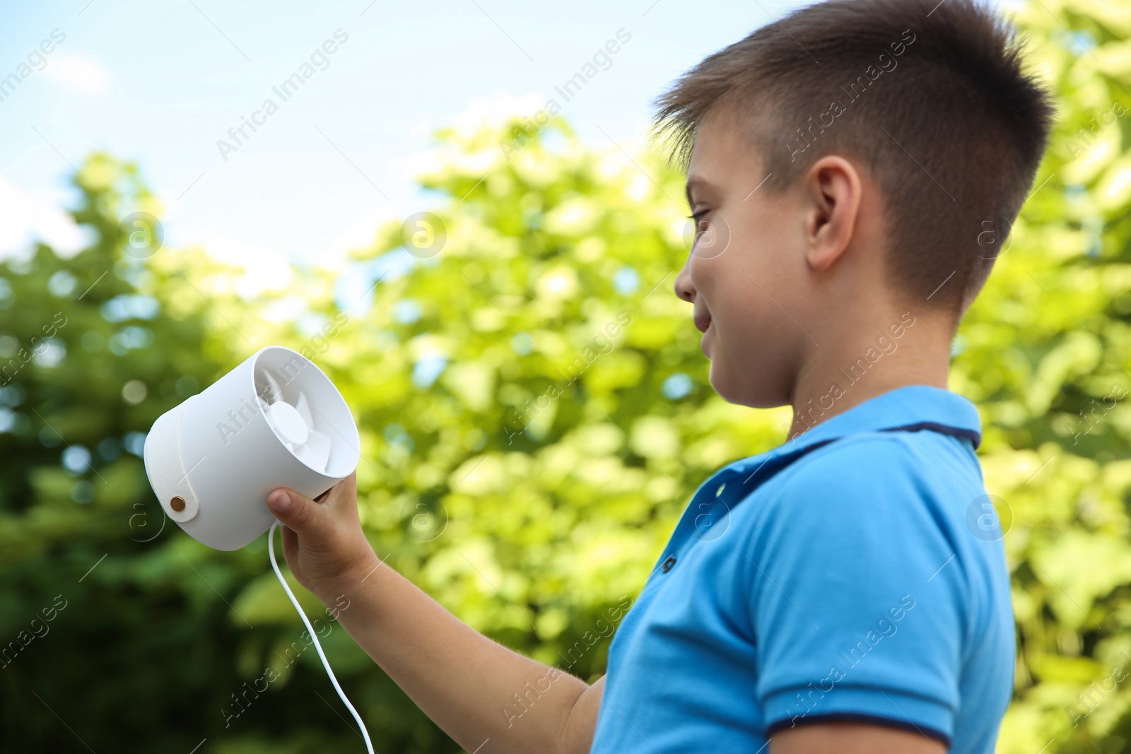 Photo of Little boy with portable fan outdoors. Summer heat