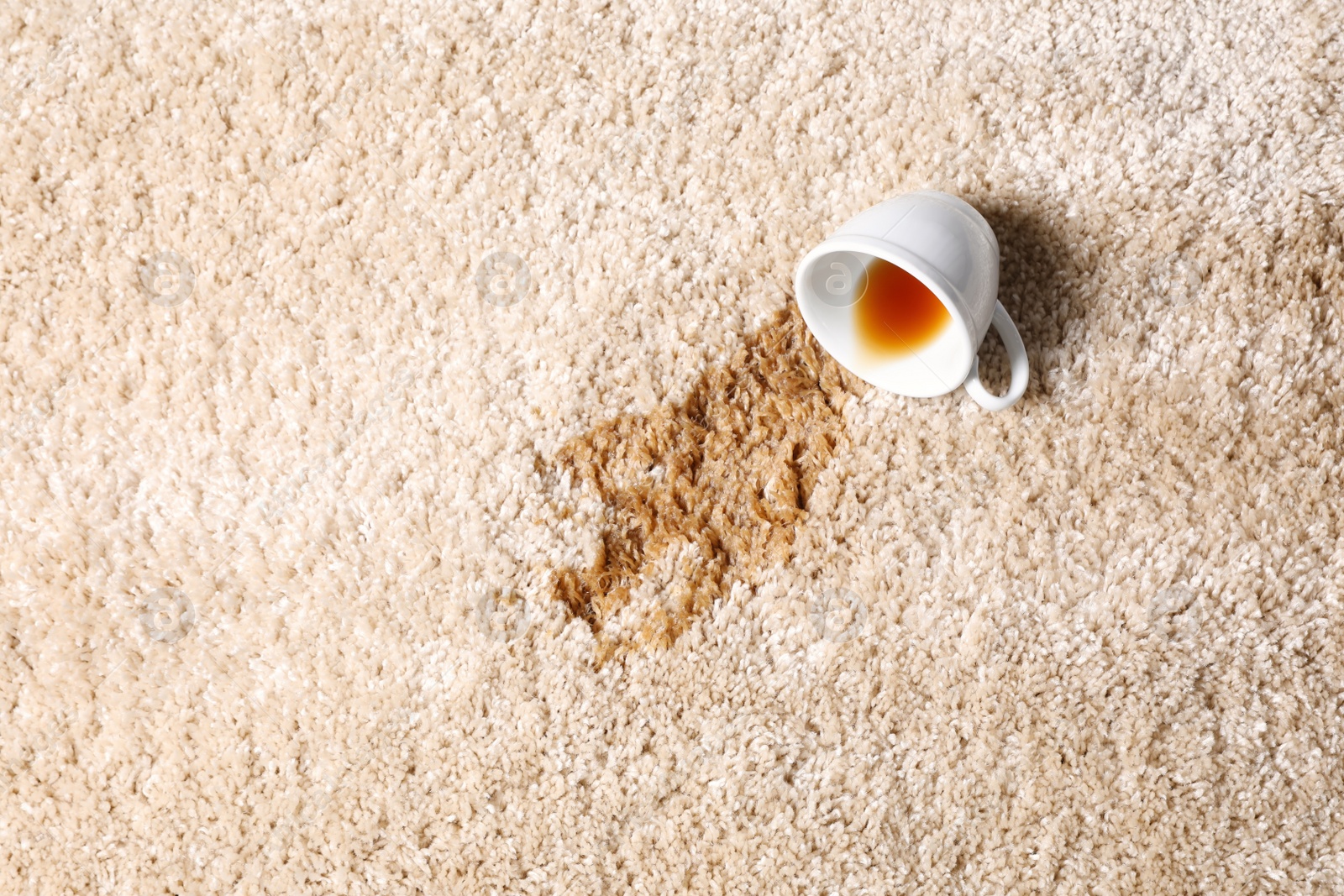 Photo of Overturned cup and spilled tea on beige carpet, top view. Space for text