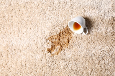 Photo of Overturned cup and spilled tea on beige carpet, top view. Space for text