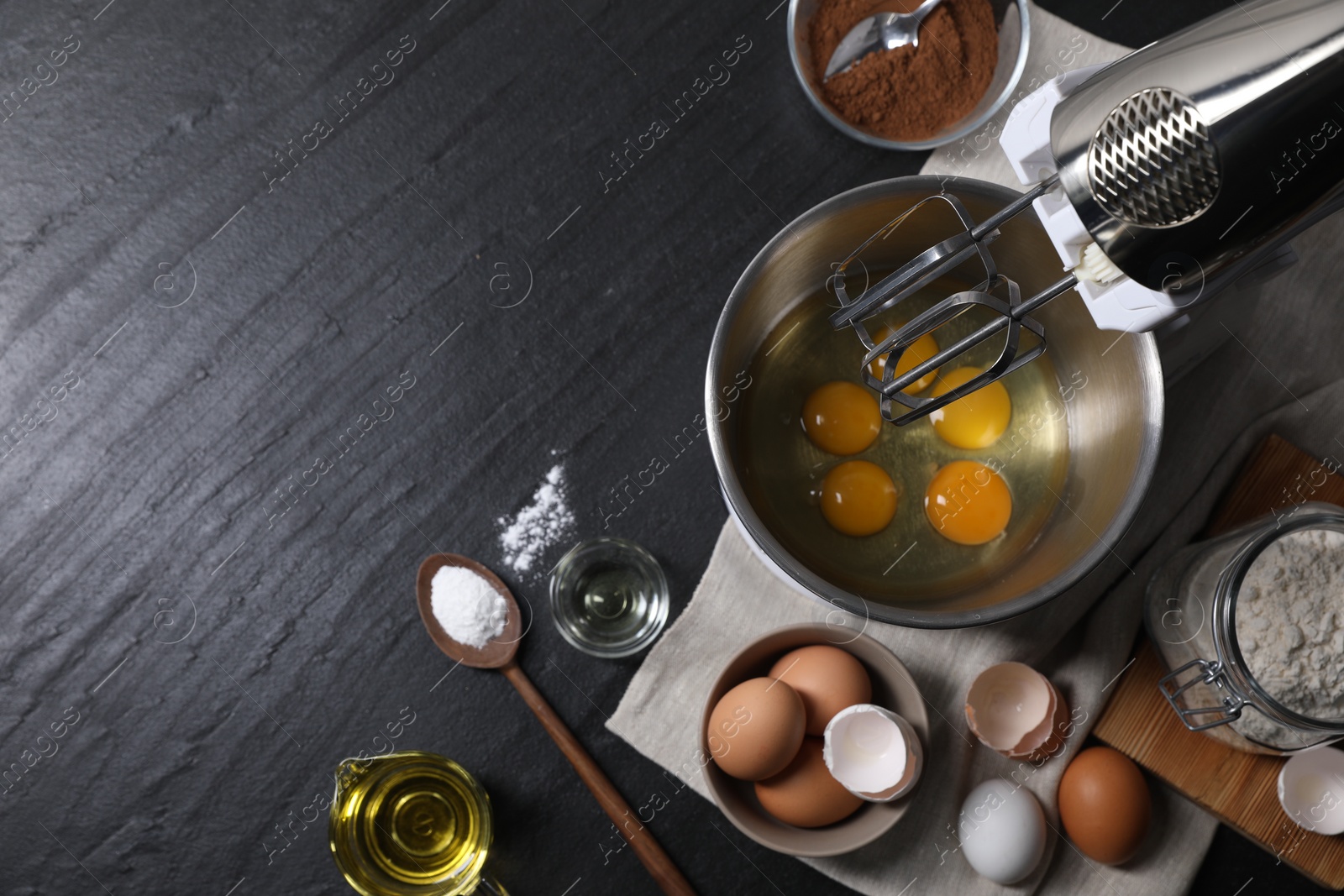 Photo of Making dough. Raw eggs in bowl of stand mixer and ingredients on black table, flat lay with space for text