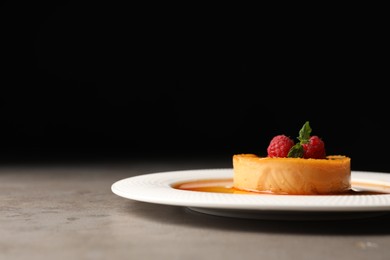 Photo of Delicious pudding with caramel and raspberries on grey table against black background. Space for text