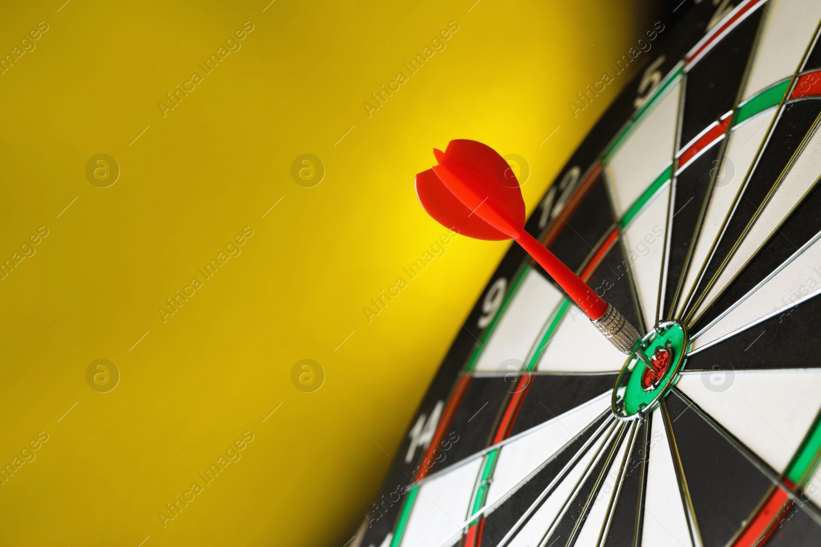 Photo of Red arrow hitting target on dart board against yellow background. Space for text