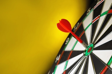 Photo of Red arrow hitting target on dart board against yellow background. Space for text