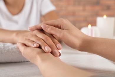 Photo of Cosmetologist massaging woman's hand at table in spa salon, closeup