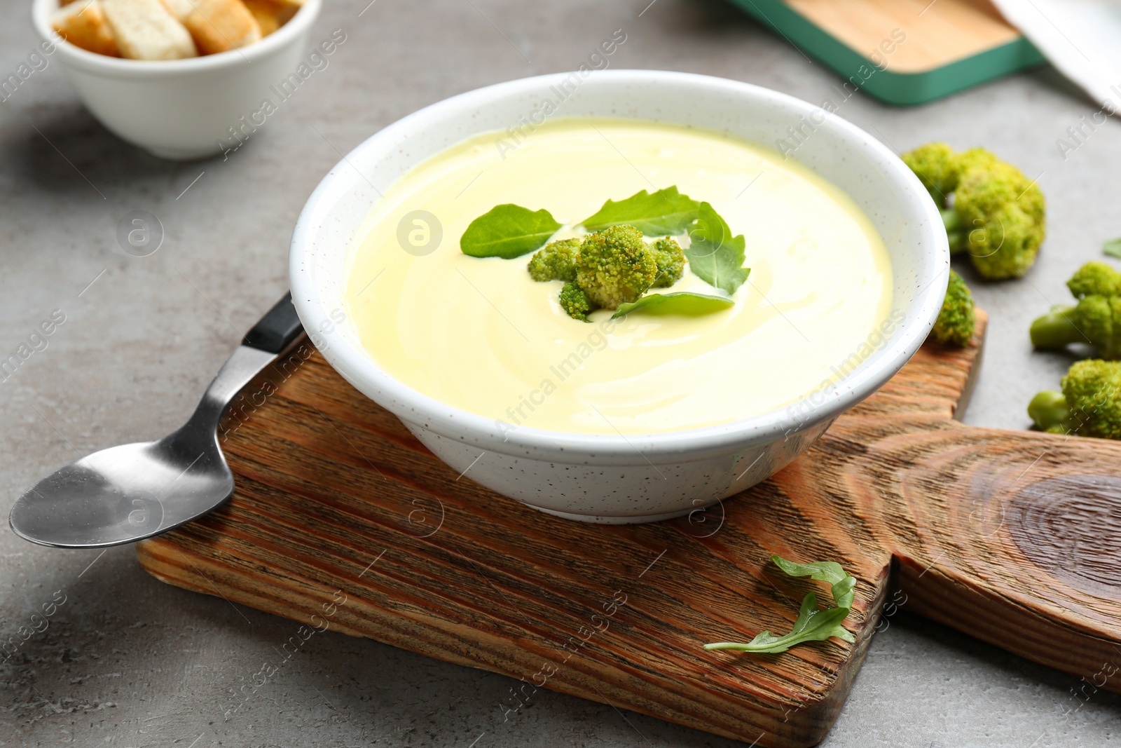 Photo of Bowl of cheese cream soup with broccoli served on grey table