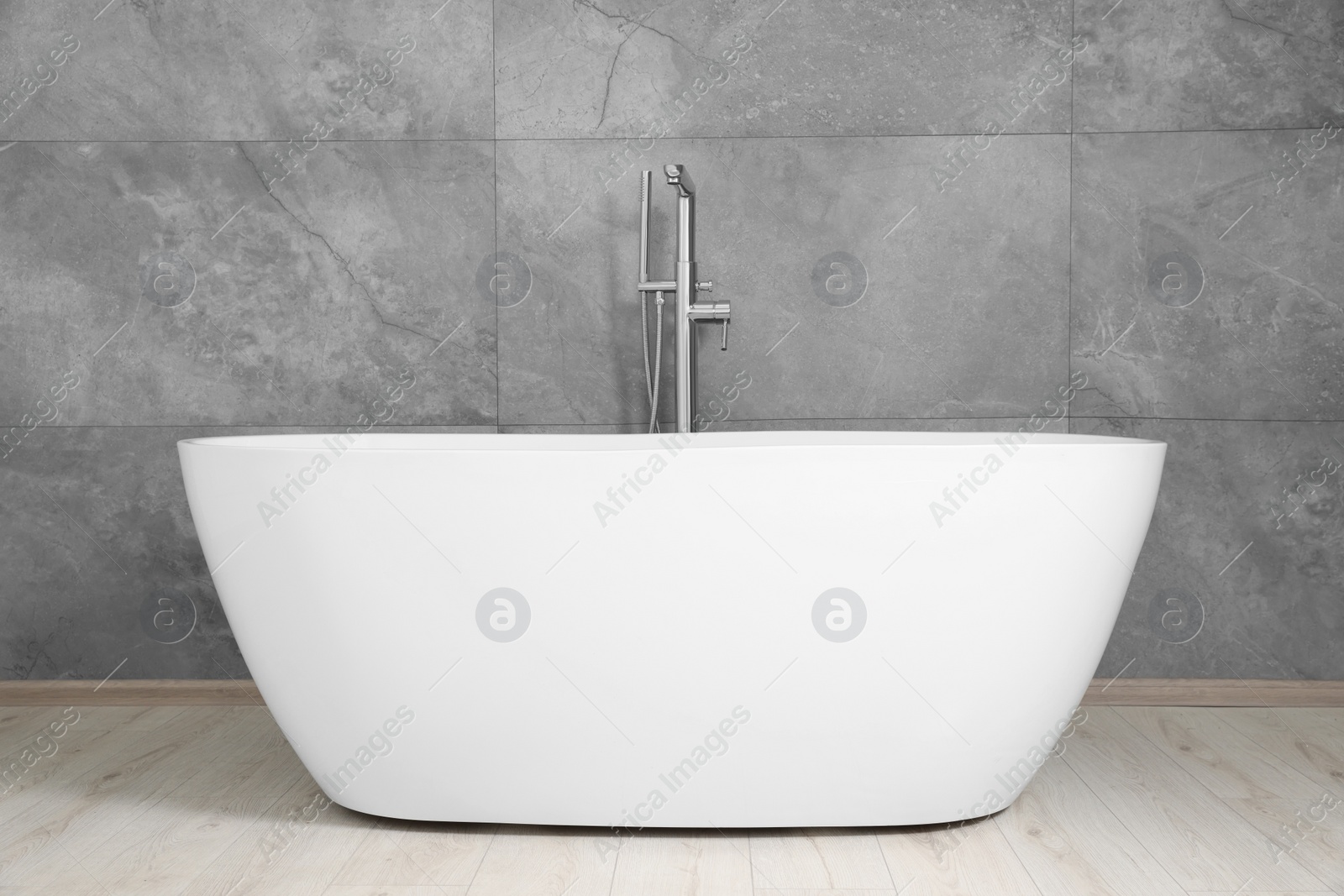 Photo of Stylish ceramic tub near light grey tiled wall indoors