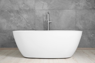 Photo of Stylish ceramic tub near light grey tiled wall indoors