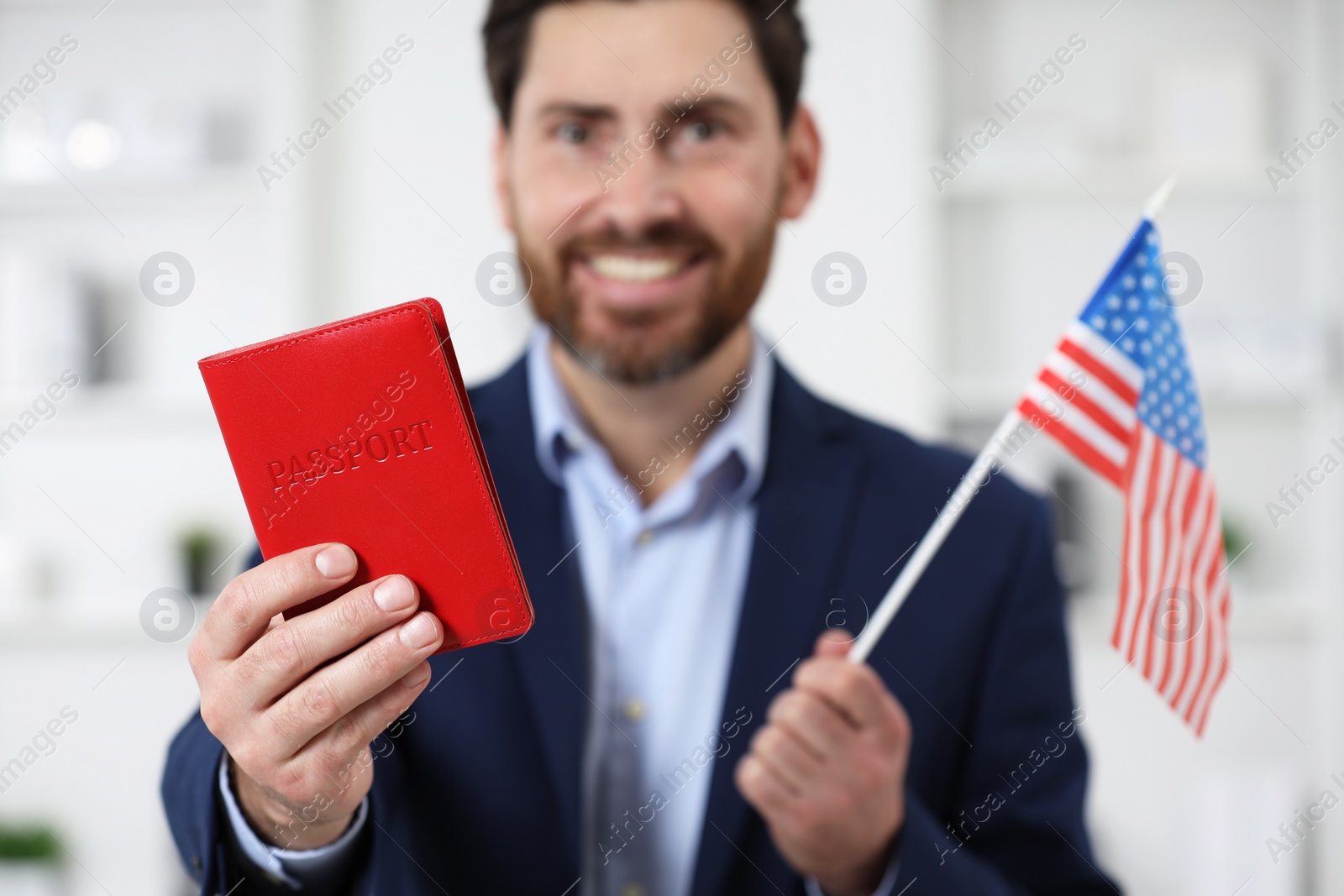 Photo of Immigration. Happy man with passport and American flag indoors, selective focus