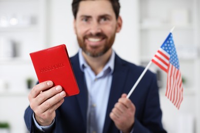 Photo of Immigration. Happy man with passport and American flag indoors, selective focus