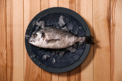 Photo of Fresh raw fish with ice on wooden table, top view