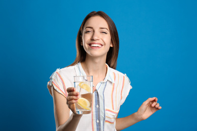 Photo of Young woman with glass of lemon water on light blue background