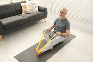 Senior man doing exercise with fitness elastic band on mat at home