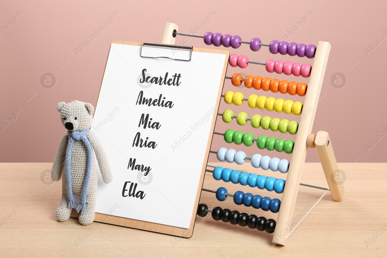 Photo of Clipboard with list of baby names and toys on wooden table