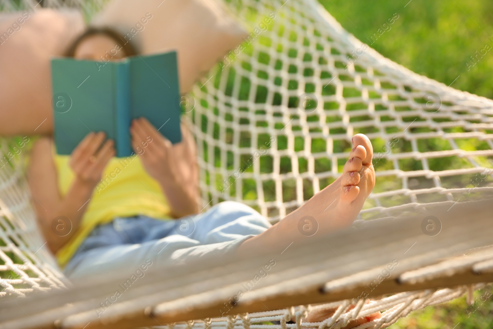 Photo of Young woman reading book in comfortable hammock at green garden