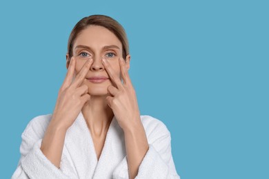 Photo of Woman massaging her face on turquoise background. Space for text