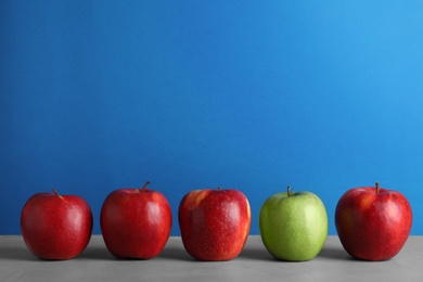 Row of red apples with green one on table against color background. Be different