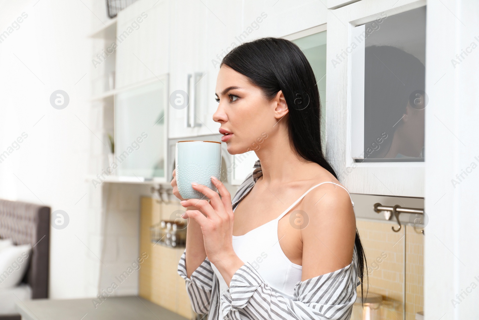 Photo of Beautiful young woman in white underwear drinking coffee at home