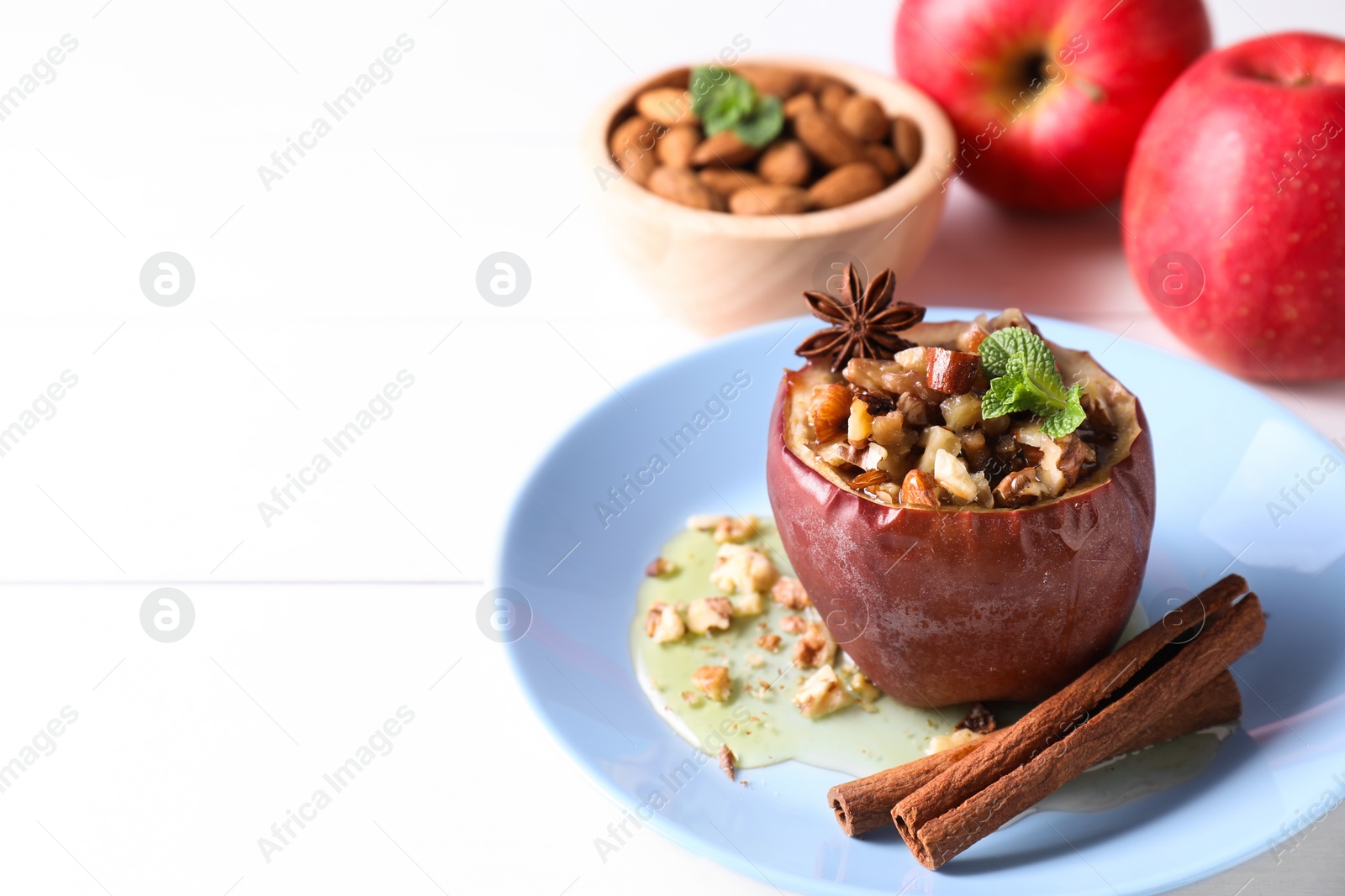 Photo of Tasty baked apple with nuts, honey, spices and mint on white wooden table