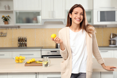 Young woman with fresh lemon in kitchen