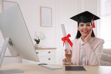 Happy student with graduation hat and diploma at workplace in office