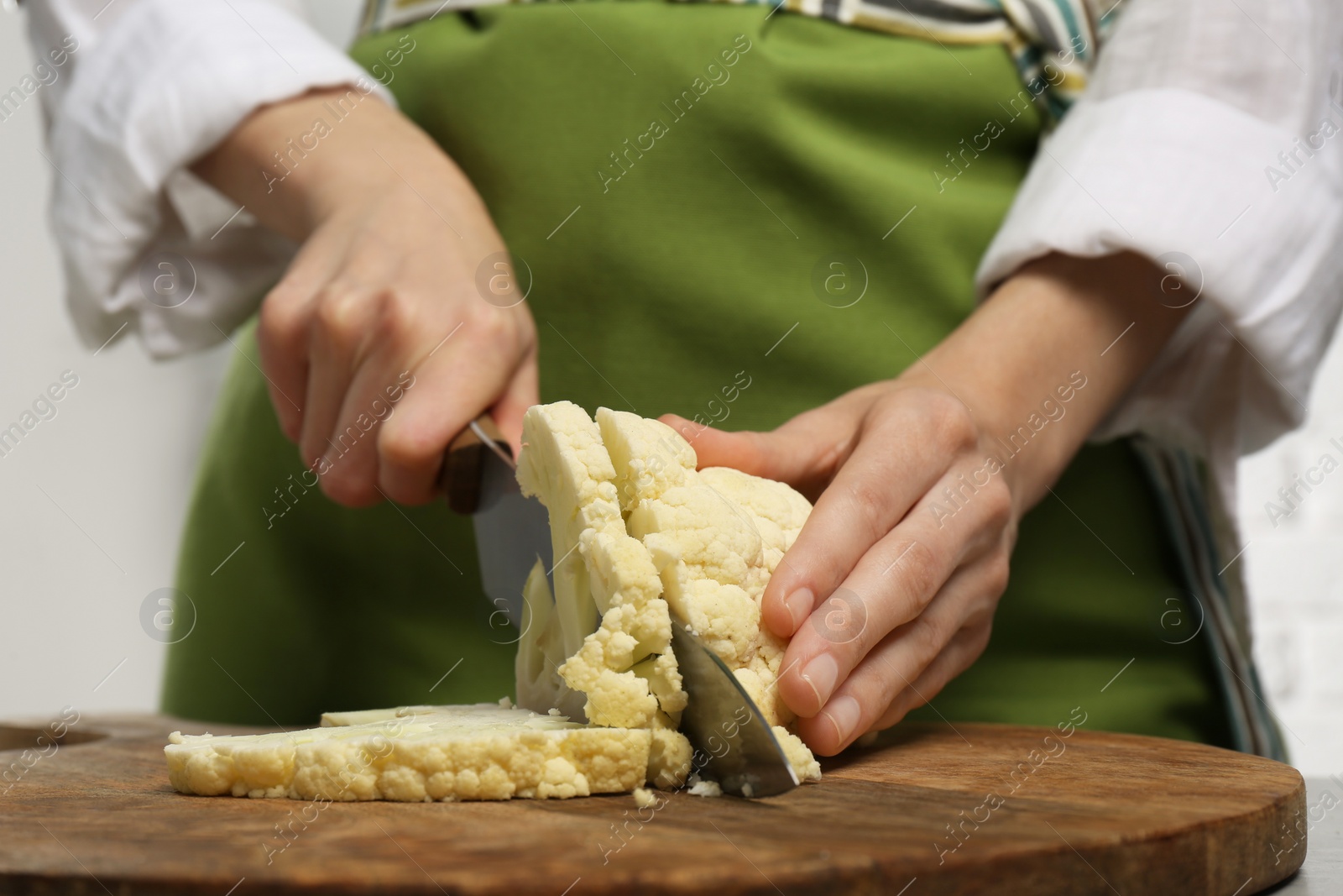 Photo of Woman cutting fresh cauliflower on wooden board, closeup