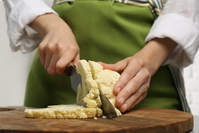 Photo of Woman cutting fresh cauliflower on wooden board, closeup